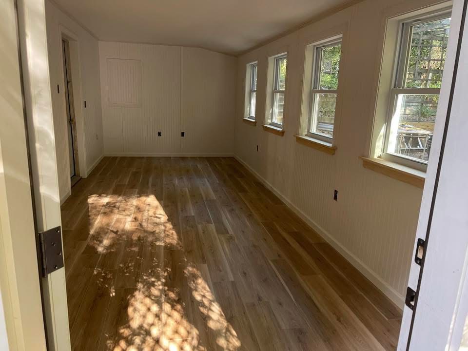 Renovated room with wood flooring, finished walls, and trimmed windows