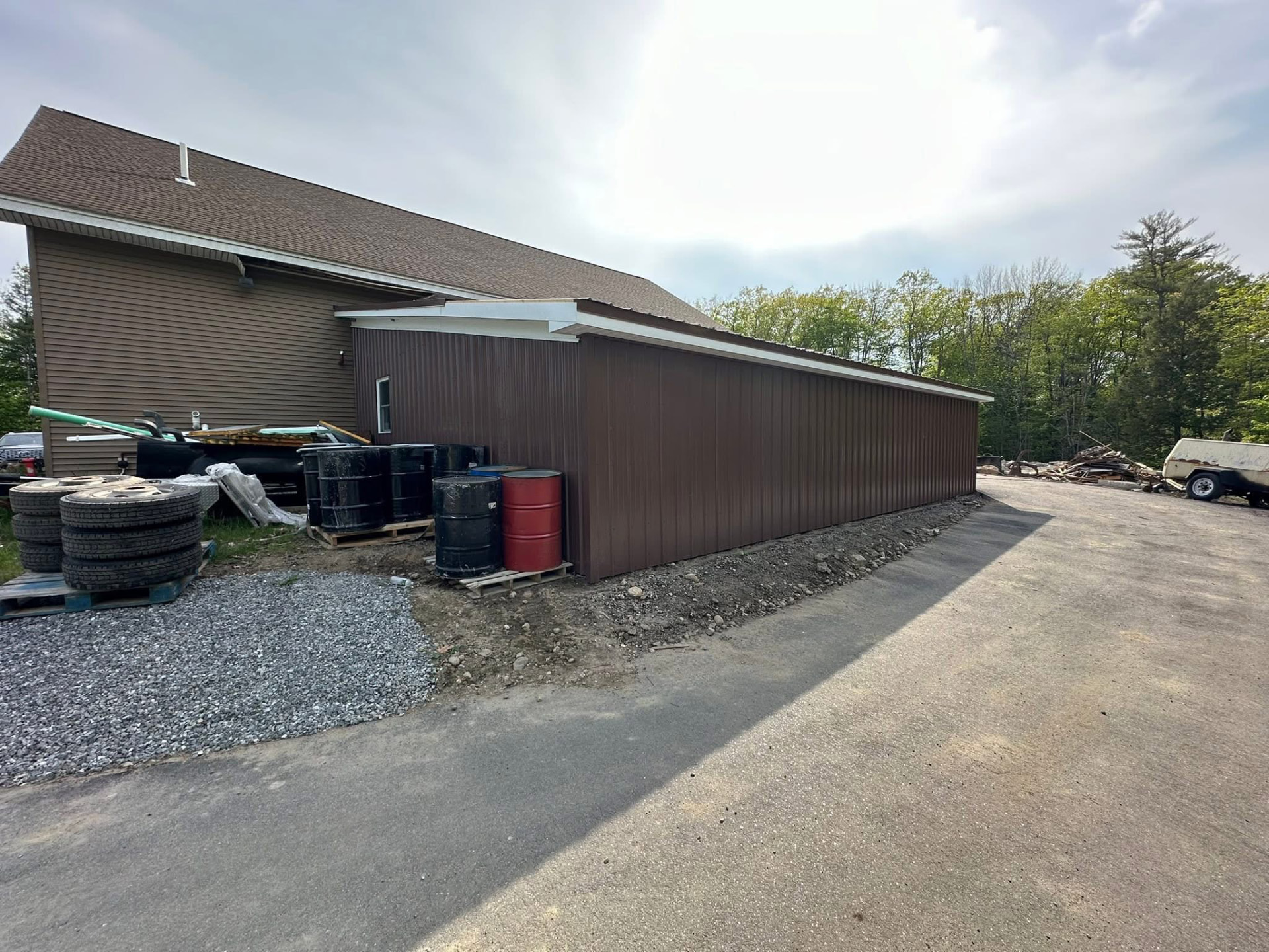 Brown metal lean-to addition with vertical ribbed siding and white trim beside an existing building
