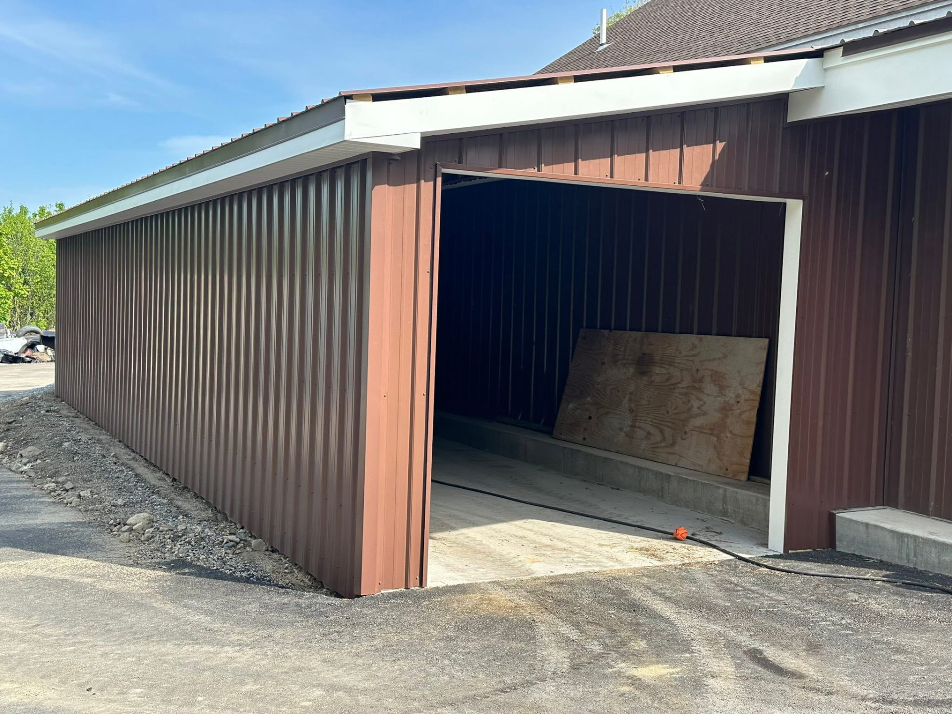 Open front of a brown metal lean-to addition with a poured concrete slab floor