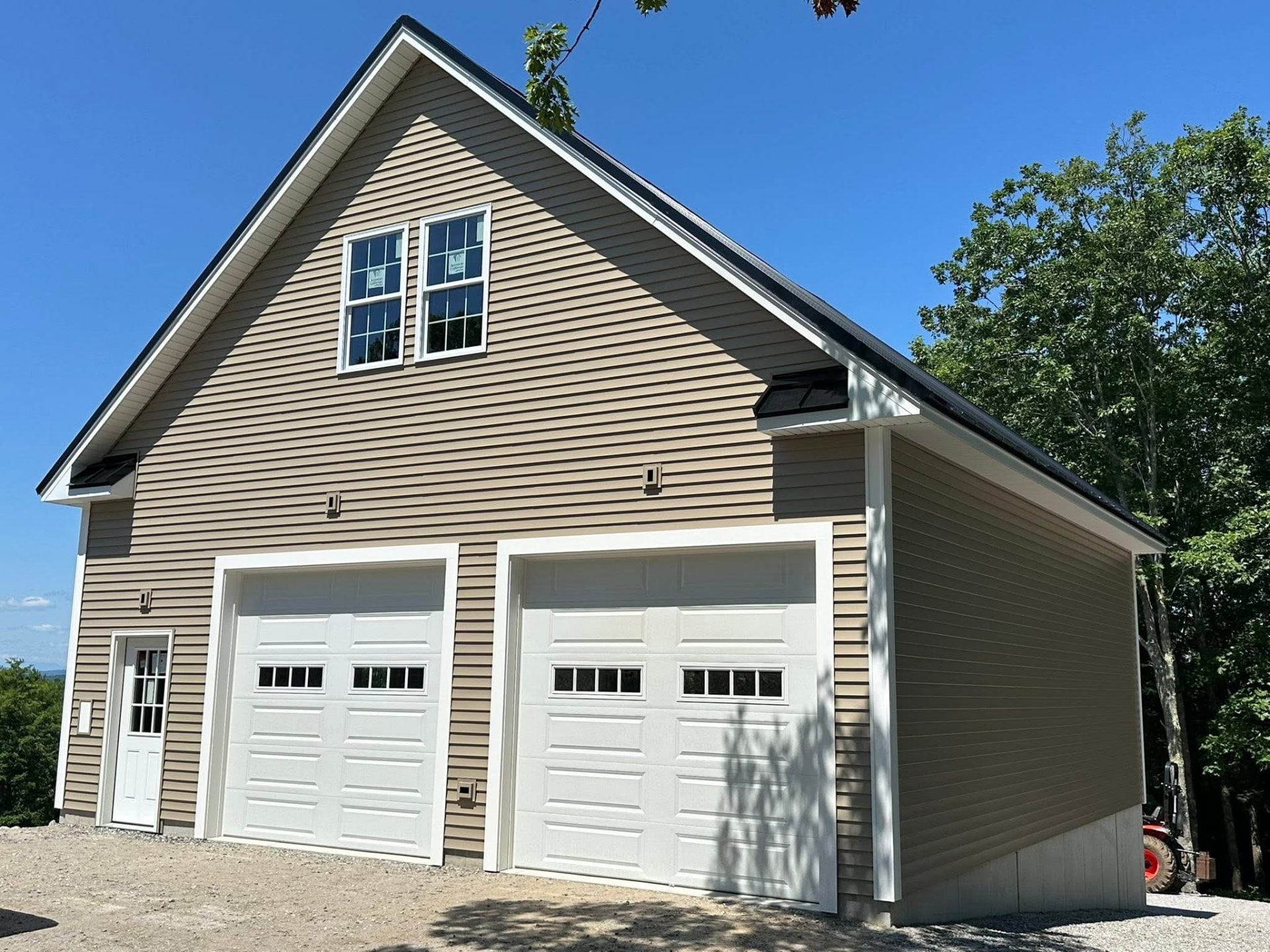 Completed two-car garage with tan siding, white trim, and black metal roof